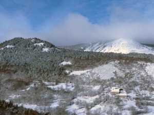 Nichée à l&#039;abri, une ferme dominée par le Mézenc dont les sommets sont habillés par les nuages.